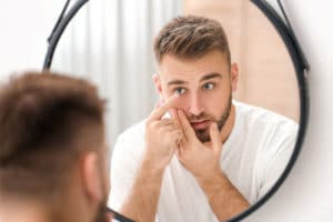 Young man putting in contact lenses near mirror.jpg